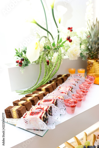Festive dessert buffet with chocolate pastries, sponge cake slices, berry mousse cups and elegant floral arrangements.