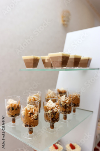 Chocolate desserts in clear glasses and layered sweet treats displayed on glass shelves at a festive buffet.