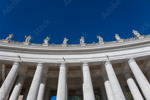 Fotografie Bernini colonnade with statues of saints against deep blue sky in St