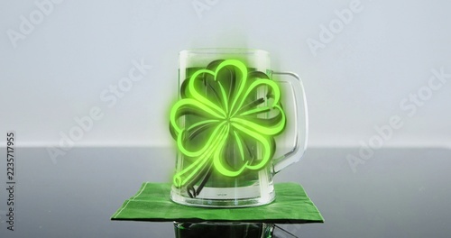 Glass mug holding glowing green shamrock light resting on coaster over gray tabletop, copy space