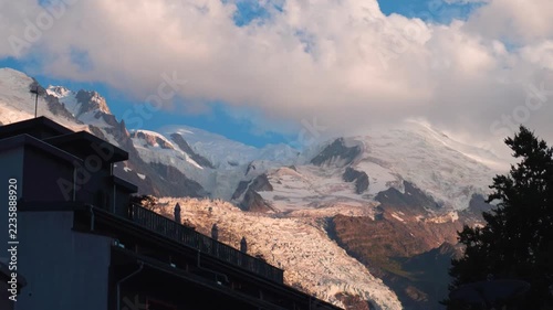Time-lapse Sunset light illuminates snowy Mont Blanc mountain peak glacier behind dark alpine building silhouette Chamonix valley French Alps summer evening