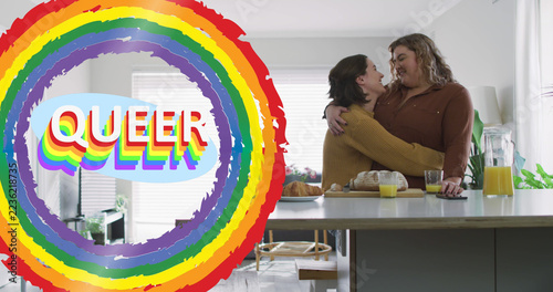 Image of rainbow and queer over lesbian couple in kitchen