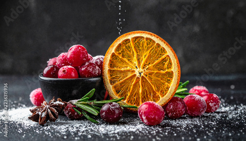 Dried orange slice and red cranberries with rosemary on dark background