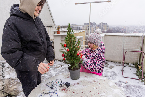 Family decorates a small Christmas tree on a snowy rooftop