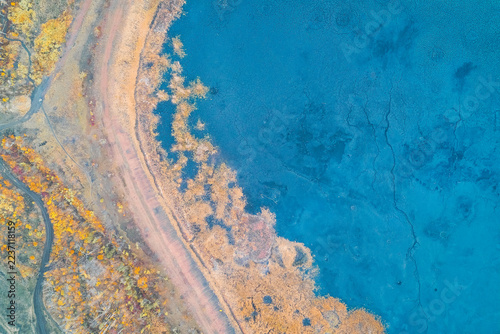 Abstract neon blue lake water and golden autumn shoreline with vibrant psychedelic textures in a drone shot