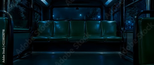 Five abreast elevated rear transit bus bench covered in dark forest green vinyl under the faint blue wash of night