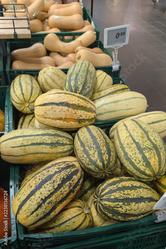 Delicata squash pumpkins are piled in green display bins at a store, with a price sign nearby, for sale ahead of Halloween